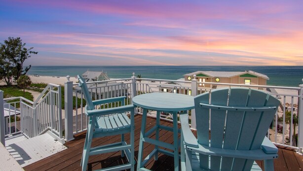 Une terrasse avec deux chaises et une table, donnant sur une plage et l’océan.