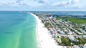 Une vue aérienne d’une ville côtière, avec une longue plage de sable, une zone résidentielle densément peuplée et une vue dégagée sur l’océan.