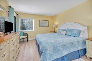 Quarto com cama, cômoda, televisão e janela com persianas.