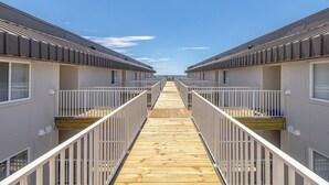 Un passage menant à une plage, bordé de part et d’autre d’immeubles à deux étages, chacun doté de balcons et de garde-corps.