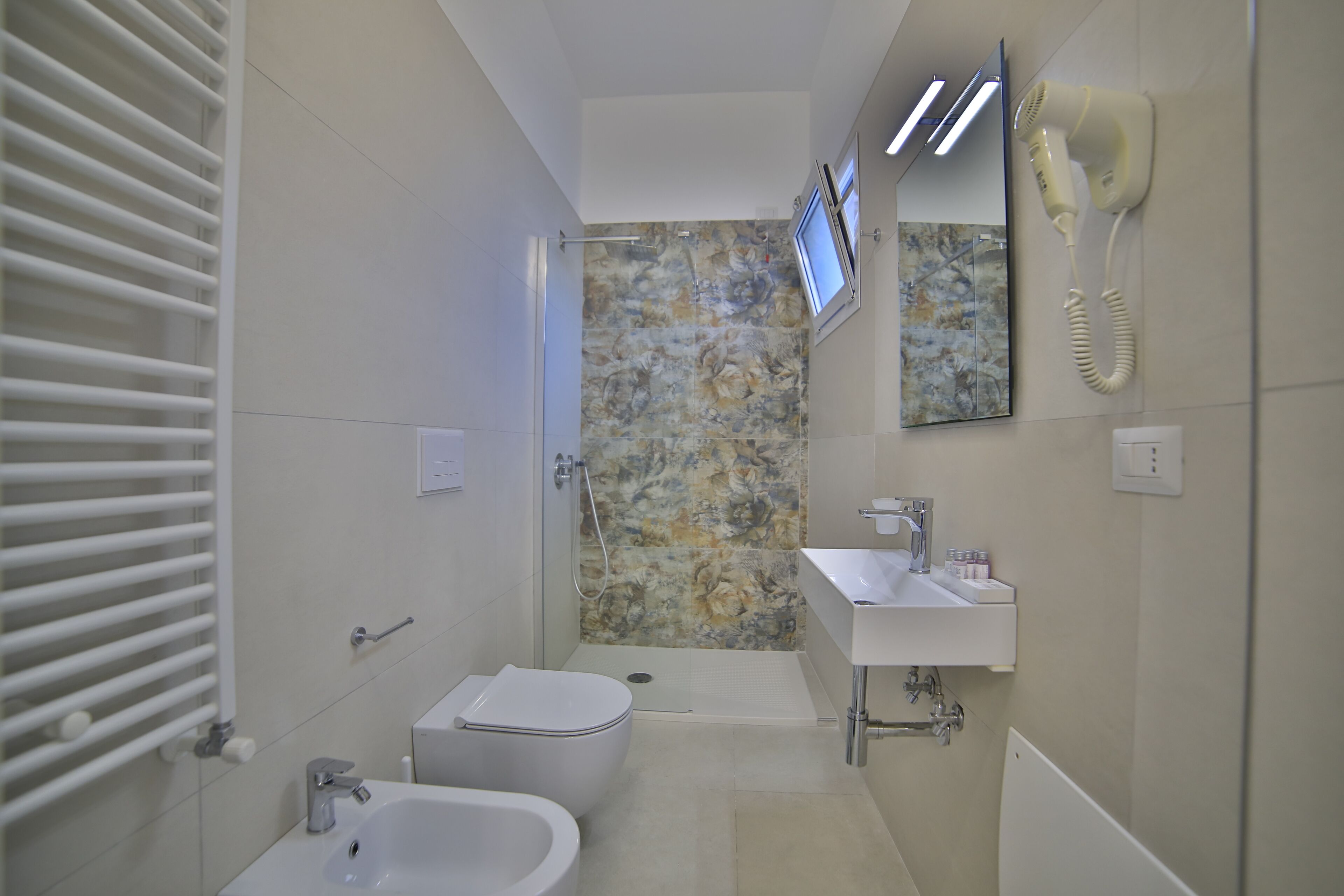 Une salle de bain équipée d’une douche, de toilettes, d’un lavabo et d’un sèche-cheveux fixé au mur.