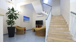 A spacious living area with a large potted plant, wicker furniture, a flat-screen TV, and a staircase. - Hotel da Ettore (Porto Cesareo)