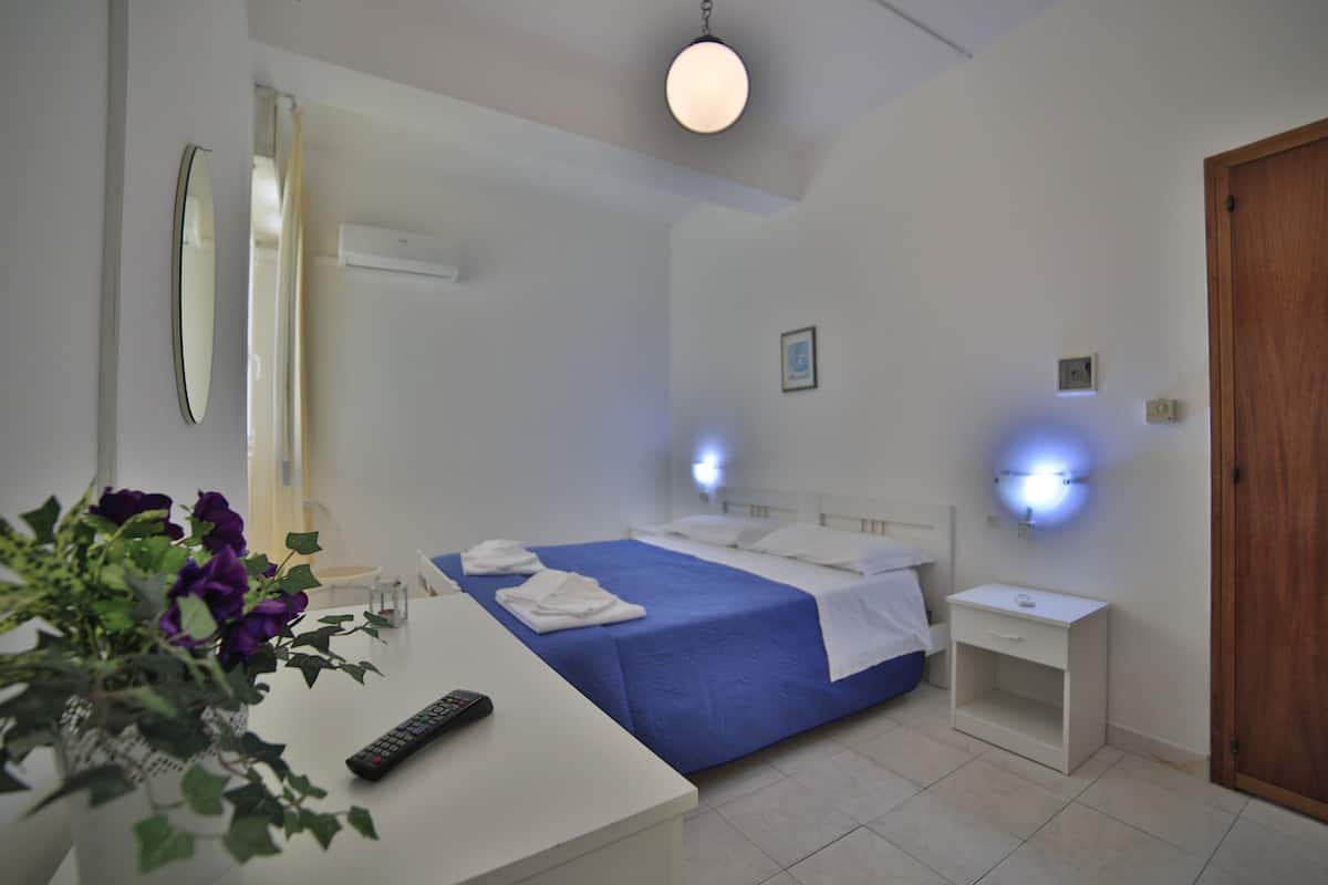 A hotel room with a bed, bedside table, and a small desk with a remote control.