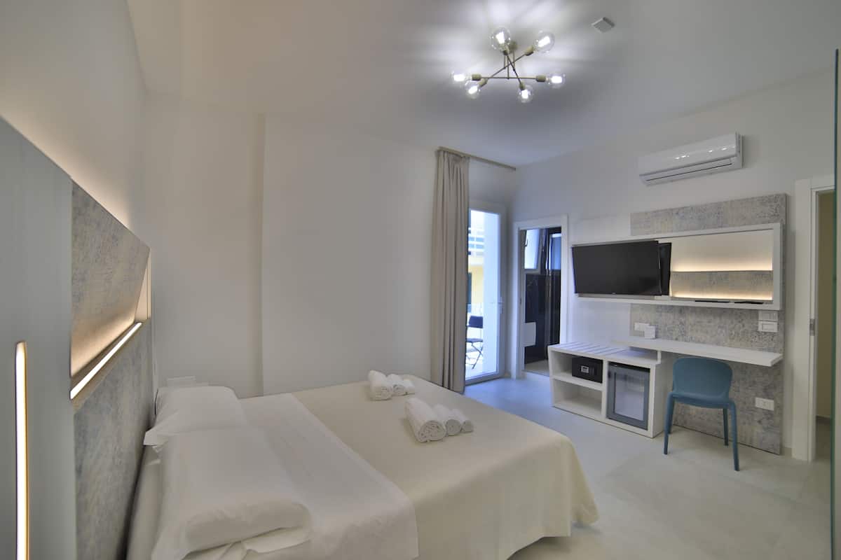 A modern hotel room with a large bed, a desk with a flat-screen TV, and a seating area.