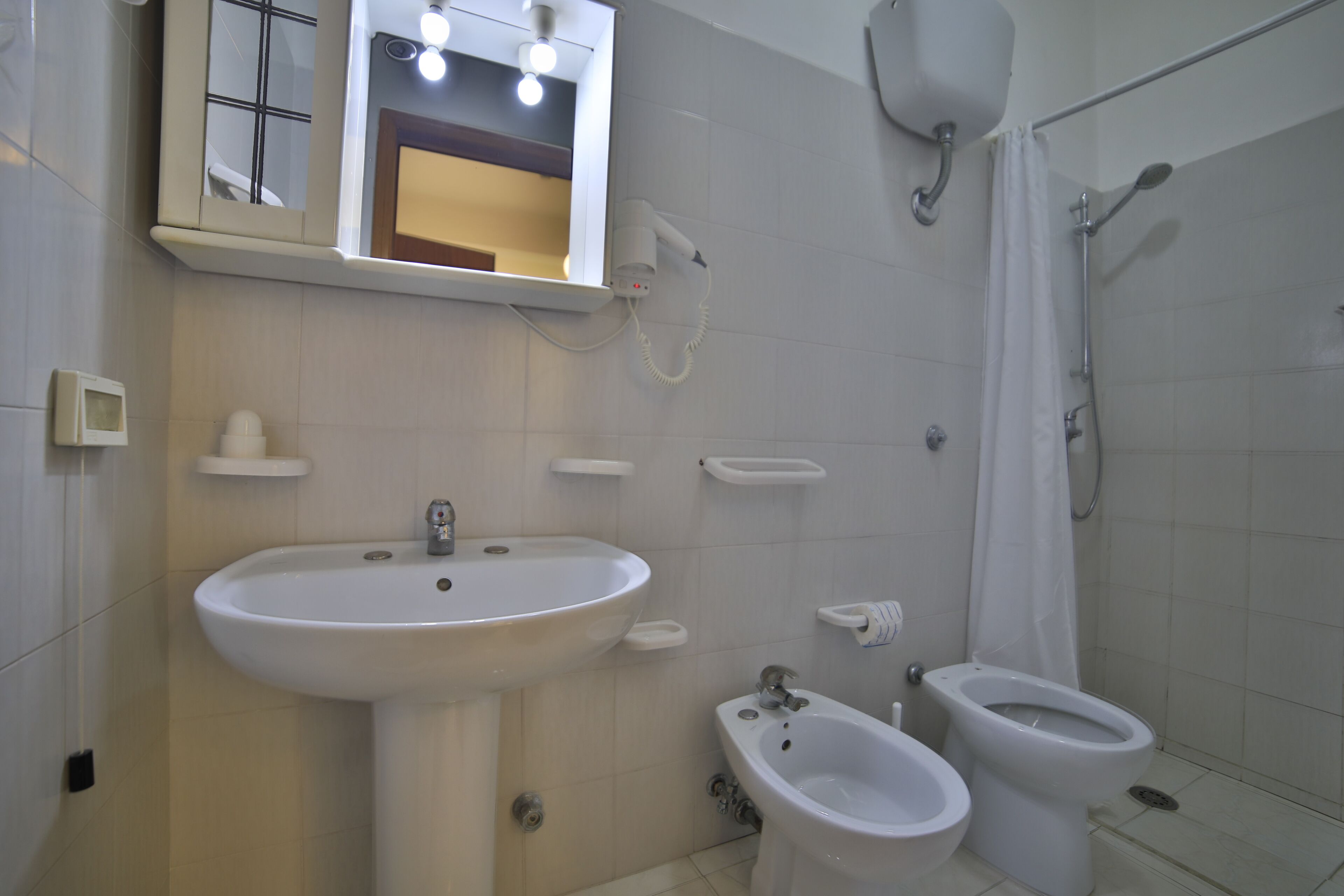 A bathroom with a sink, bidet, toilet, and a shower area.
