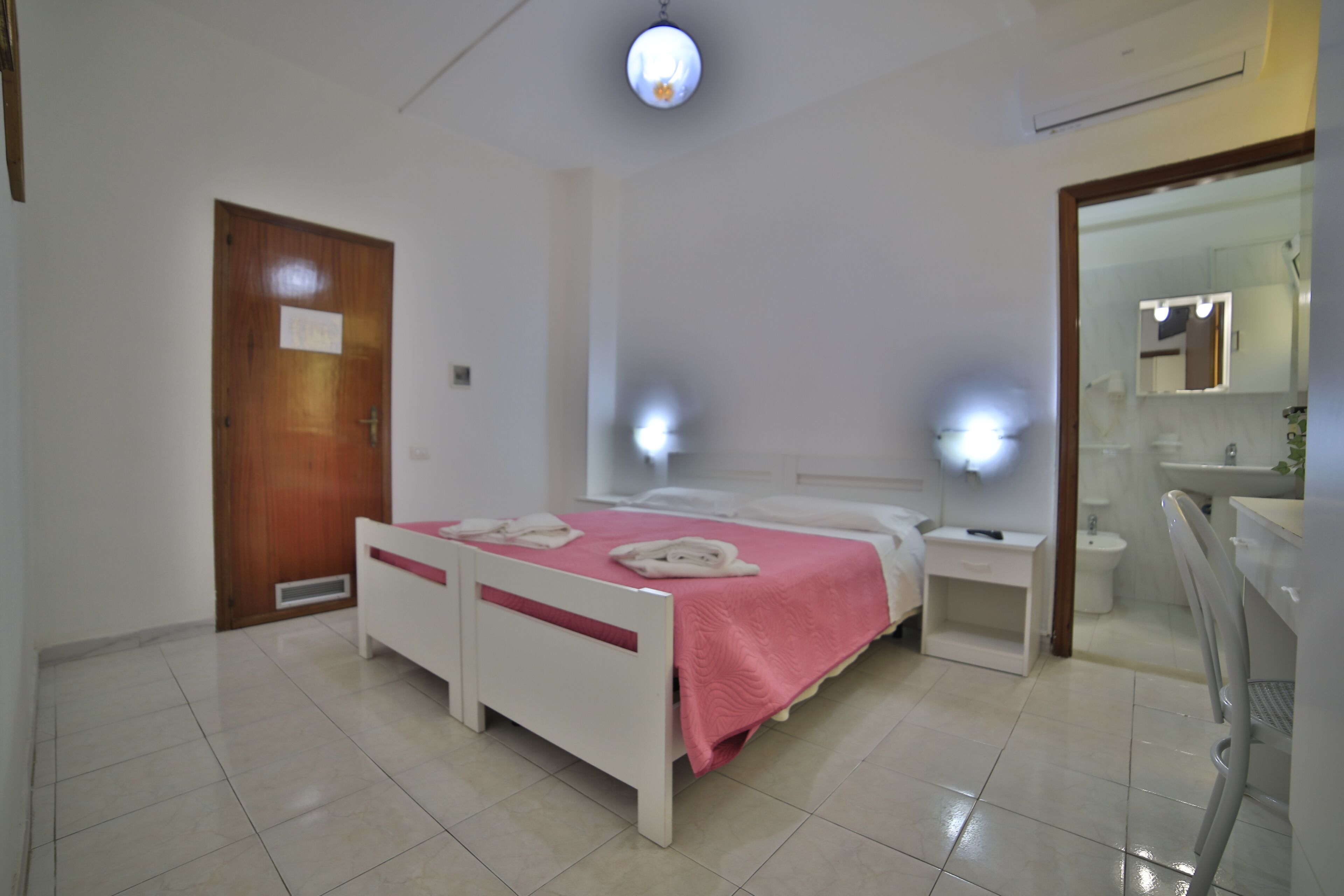 Une chambre d’hôtel comprenant un lit, des tables de chevet, un miroir et une salle de bain avec un lavabo et des toilettes.