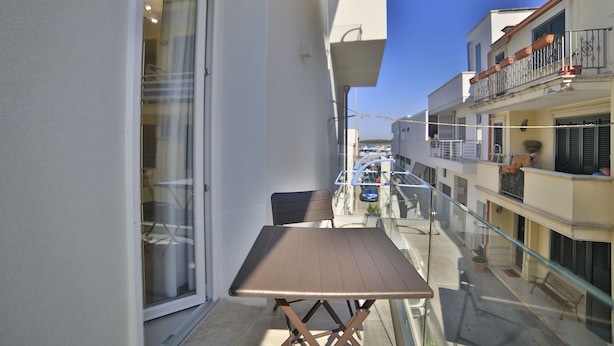 A balcony with a table and chairs, overlooking a street with parked cars and buildings. - Hotel da Ettore (Porto Cesareo)