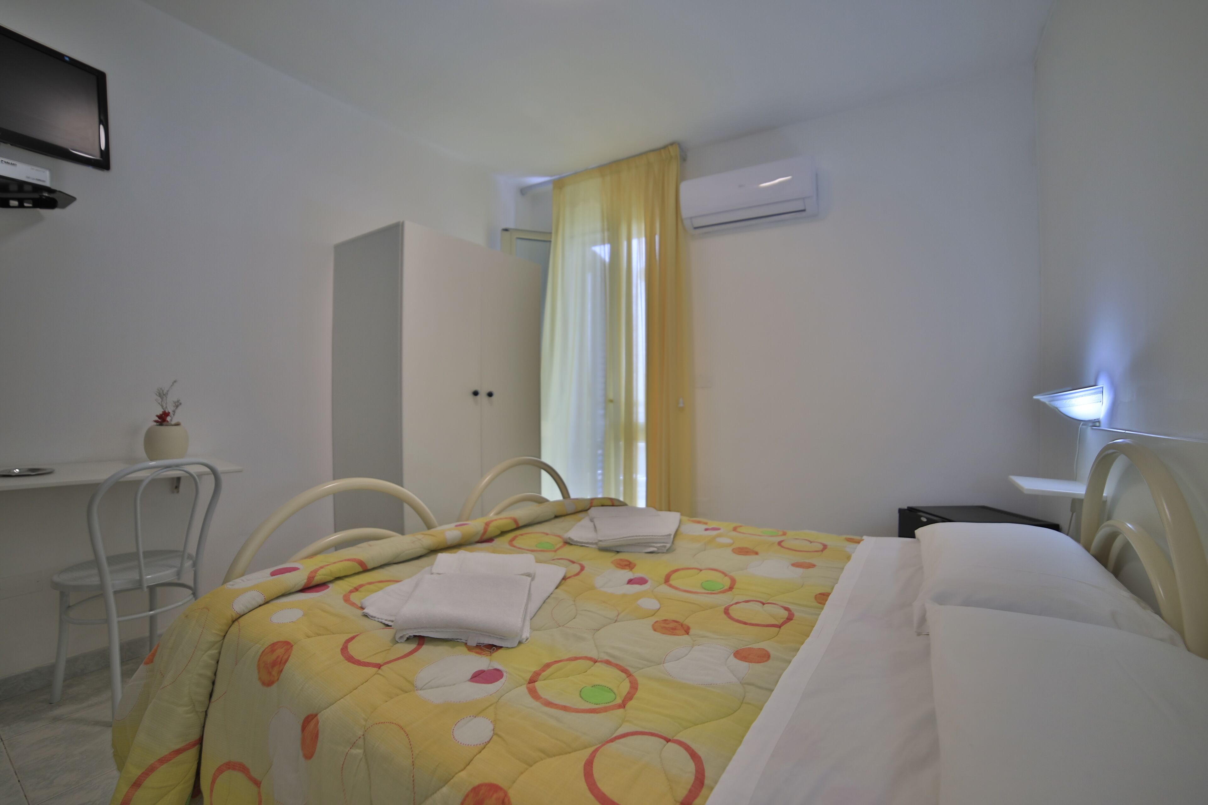 A hotel room with a bed, a desk, a chair, and a TV.