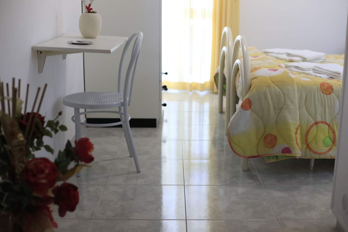 A bedroom with a bed, a chair, a desk, and a vase with flowers.