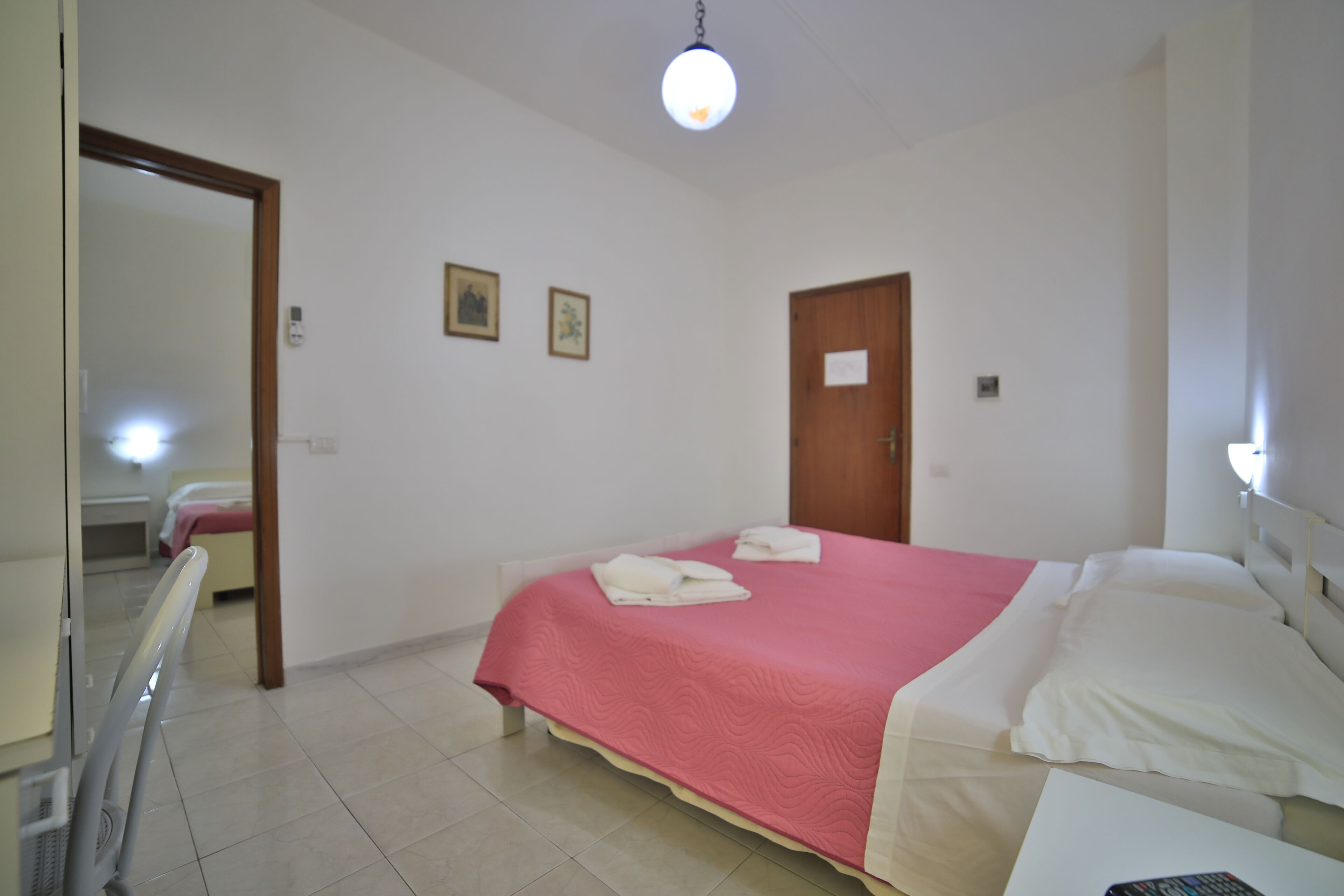 A hotel room with a bed, a bedside table, a mirror, and a door.