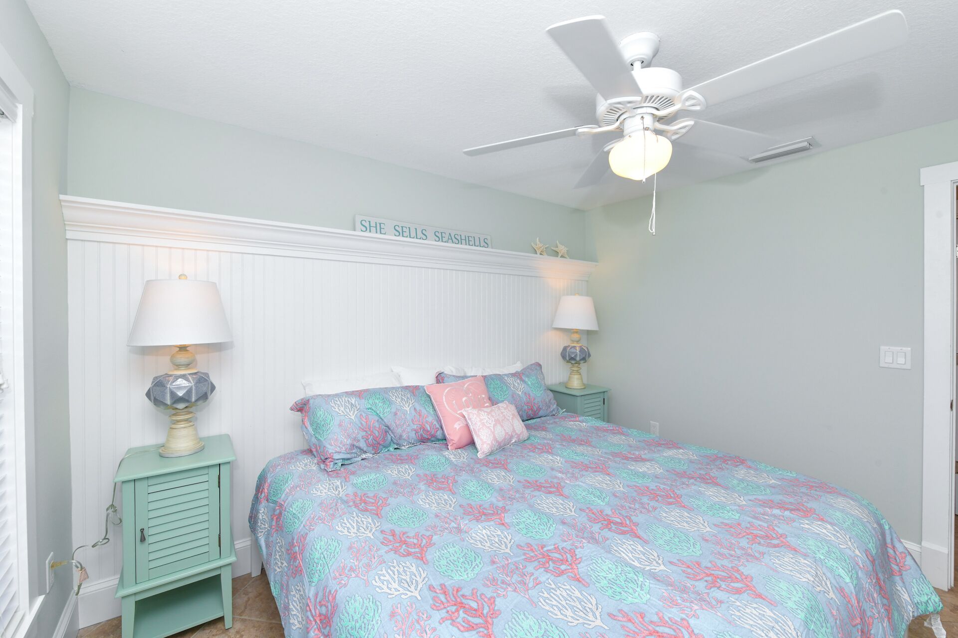 A bedroom with a bed, two bedside lamps, a ceiling fan, and a sign above the bed.