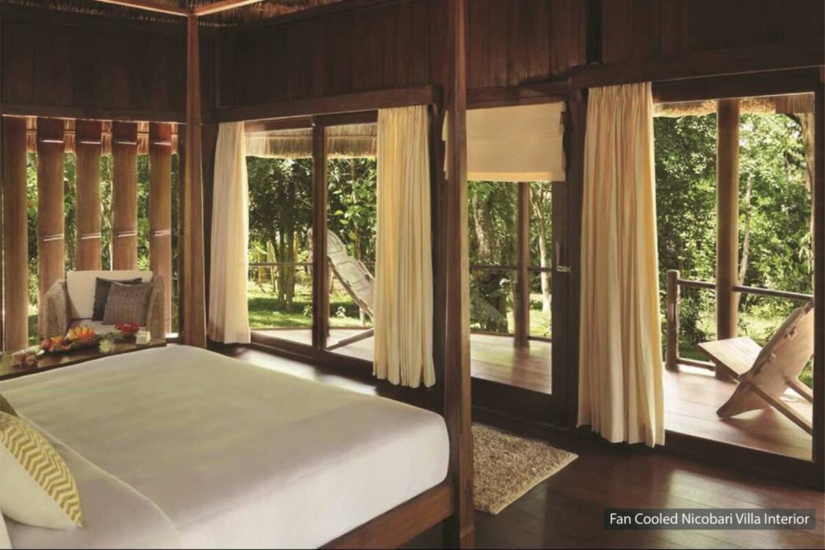 Interior de una villa con aire acondicionado, una cama grande, cortinas y vistas al verde circundante.