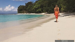 A beach with clear turquoise water and a person walking on the sand. - Barefoot at Havelock (Port Blair)