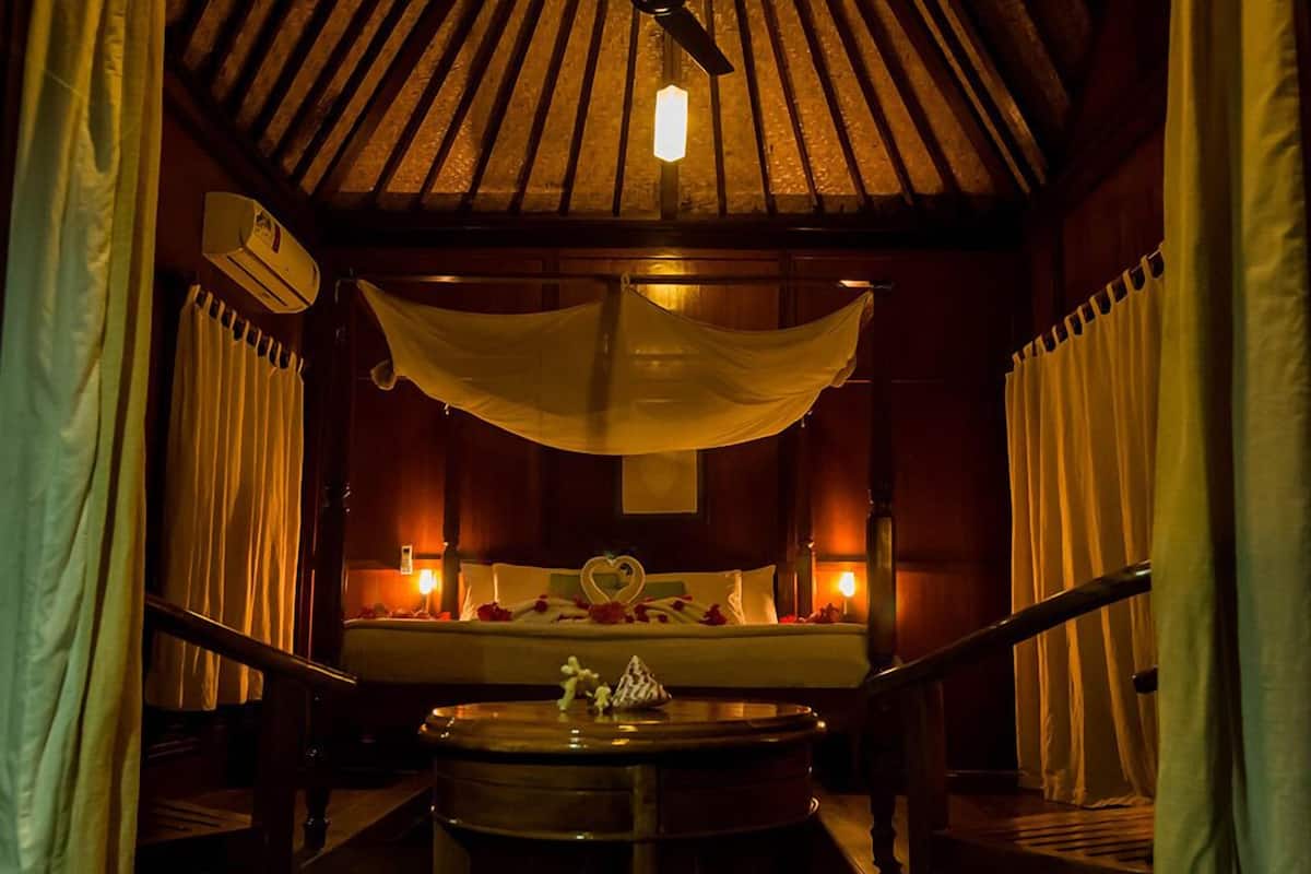 Una habitación con poca luz, una cama, una mesa redonda y un ventilador de techo.