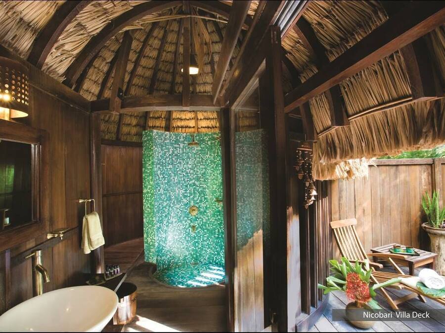 A bathroom with a green mosaic wall, wooden beams, and a thatched roof.