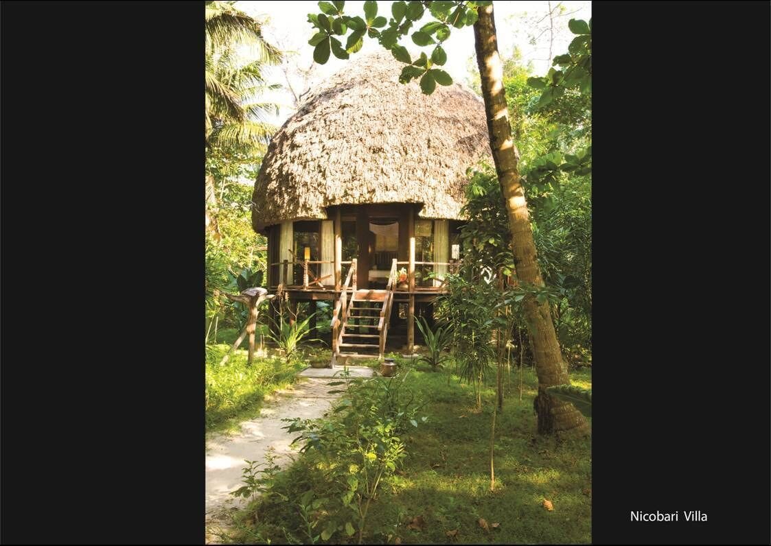Eine Villa mit Reetdach, einer Holterrasse und einer Leiter zum Eingang, umgeben von üppiger Vegetation.