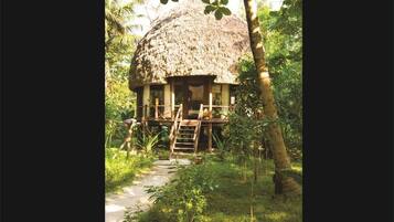 Eine Villa mit Reetdach, einer Holterrasse und einer Leiter zum Eingang, umgeben von üppiger Vegetation.