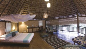 A room with a thatched roof, a bed with a canopy, a table with chairs, and a view of the ocean. - Barefoot at Havelock (Port Blair)