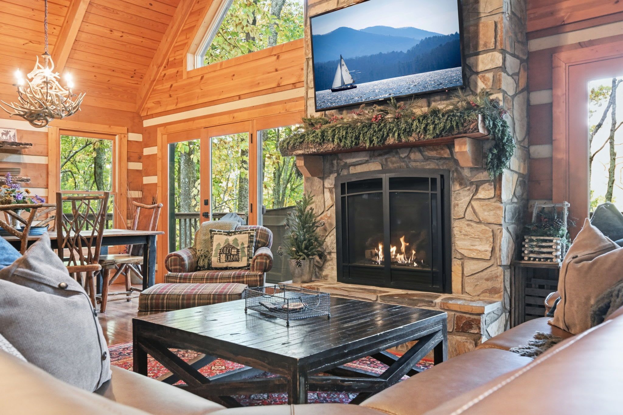 A cozy cabin interior with a stone fireplace, comfortable seating, and a television mounted above the fireplace.