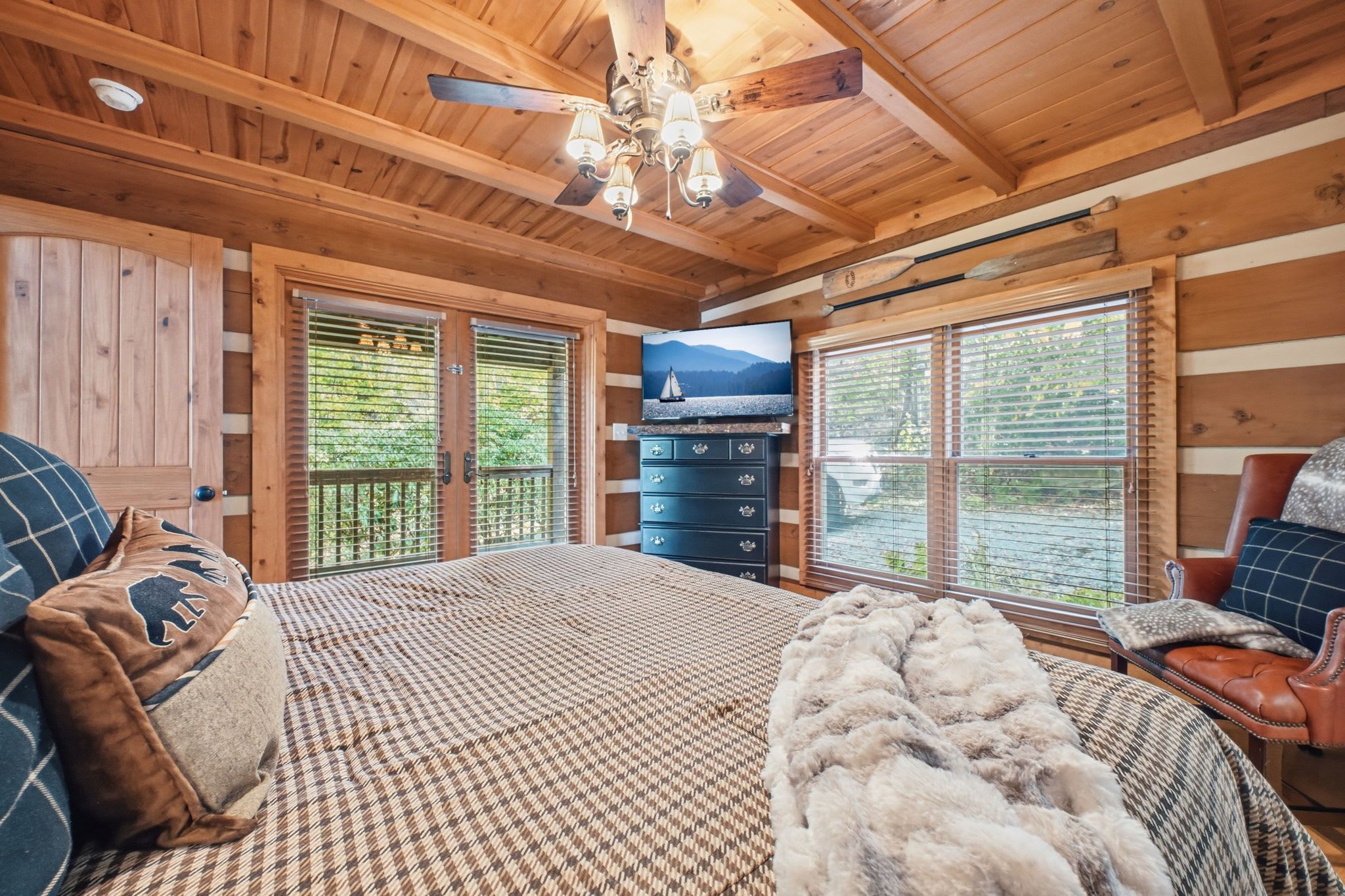 A wooden cabin bedroom with a bed, dresser, and a TV on the wall.