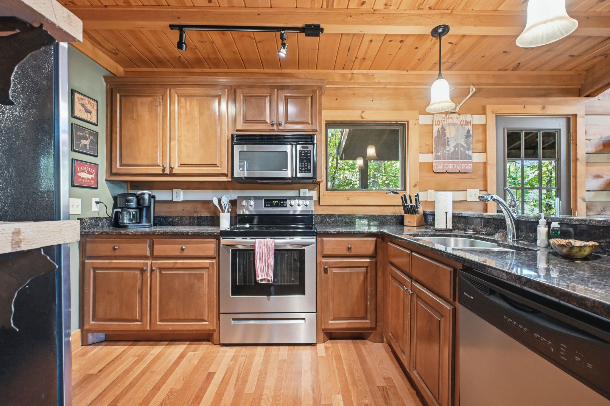 A kitchen with wooden cabinets, stainless steel appliances, a granite countertop, and a window with a view of greenery.
