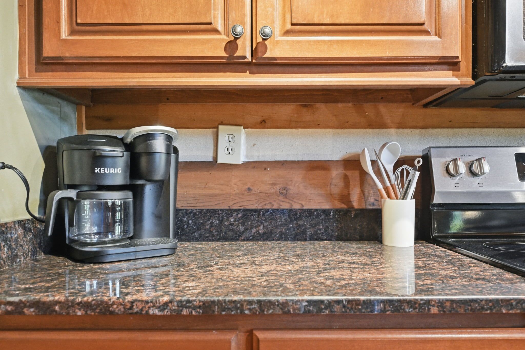 A kitchen with a Keurig coffee maker, a white mug, and a container with utensils.
