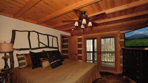 A bedroom with a bed, a wooden ceiling, a chandelier, a dresser, and a view of a field through a door. - Luxury Cabin: 3 Kings, Hot Tub, Fireplace, Lg Deck (Banner Elk)