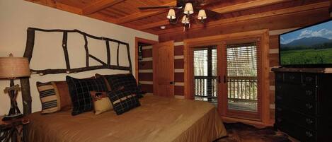 Un dormitorio con cama, techo de madera, candelabro, cómoda y vista a un campo a través de una puerta.