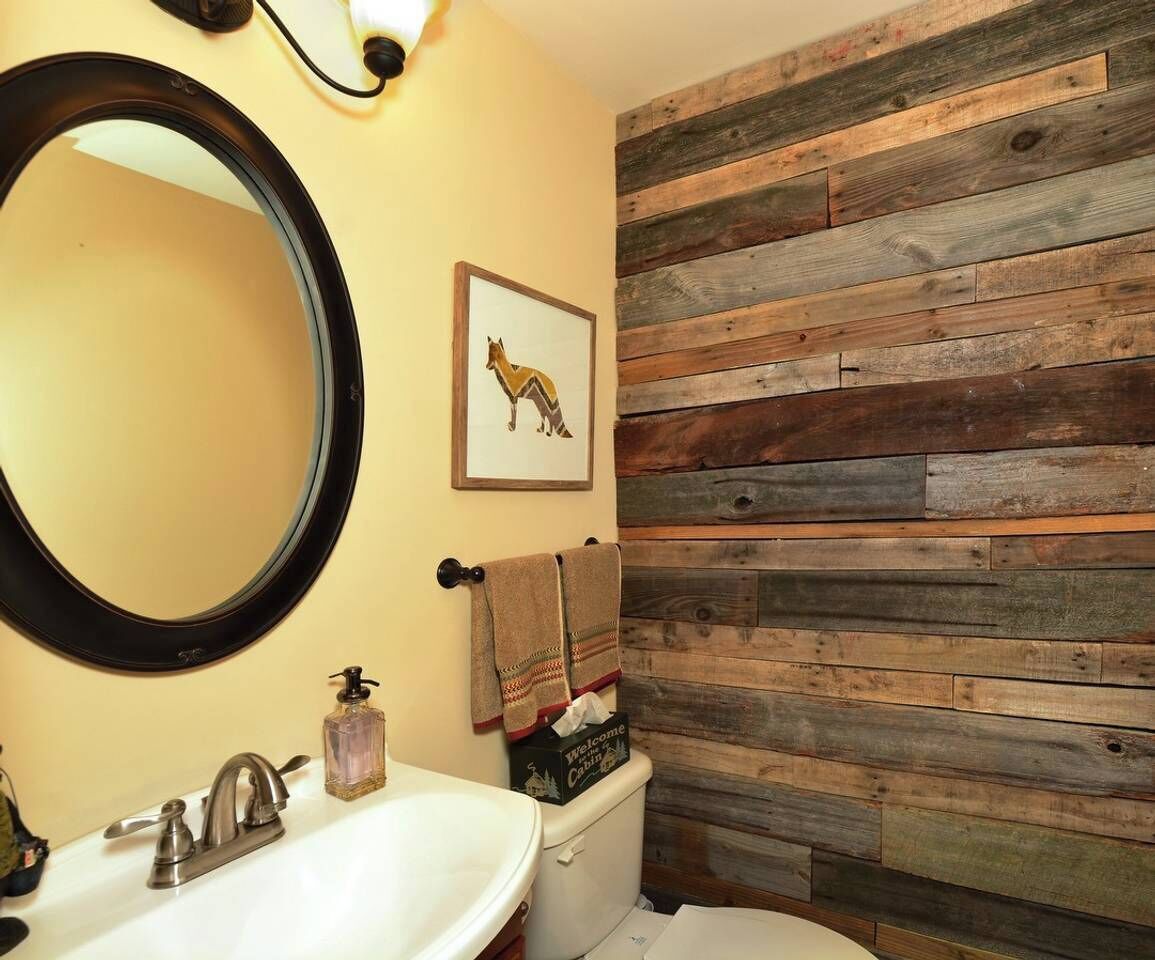 Un baño con un panel de pared de madera, un espejo redondo, un lavamanos y un inodoro.