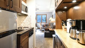 Una cocina equipada con refrigerador, estufa, microondas y cafetera. Se aprecia una ventana al fondo y un área de descanso con mesa y sillas.