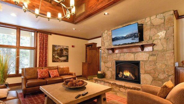 Una sala de estar acogedora con chimenea de piedra, un televisor de pantalla plana grande montado en la pared, sofás de cuero y techo de madera.