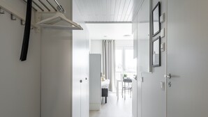 A narrow hallway with white walls, a ceiling with wooden panels, and a door leading to a room with a bed and a table. - Hiisi Homes Turku Fleminginkatu (Turku)