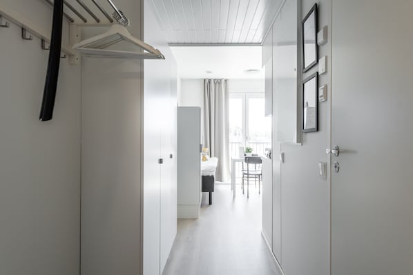 A narrow hallway with white walls, a ceiling with wooden panels, and a door leading to a room with a bed and a table. - Hiisi Homes Turku Fleminginkatu (Turku)