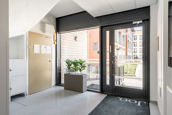 Una entrada de hotel moderna con puerta de vidrio, un mostrador de recepción y una planta en maceta.