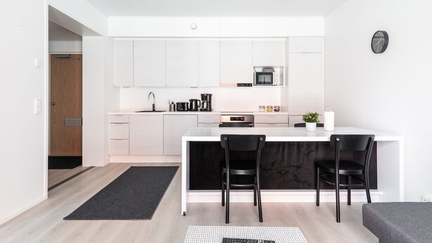 A modern kitchen with white cabinets, a black countertop, and two black chairs. - Hiisi Homes Turku Fleminginkatu (Turku)