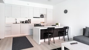 A modern kitchen with white cabinets, a central island with chairs, a microwave, and a coffee maker. - Hiisi Homes Turku Fleminginkatu (Turku)