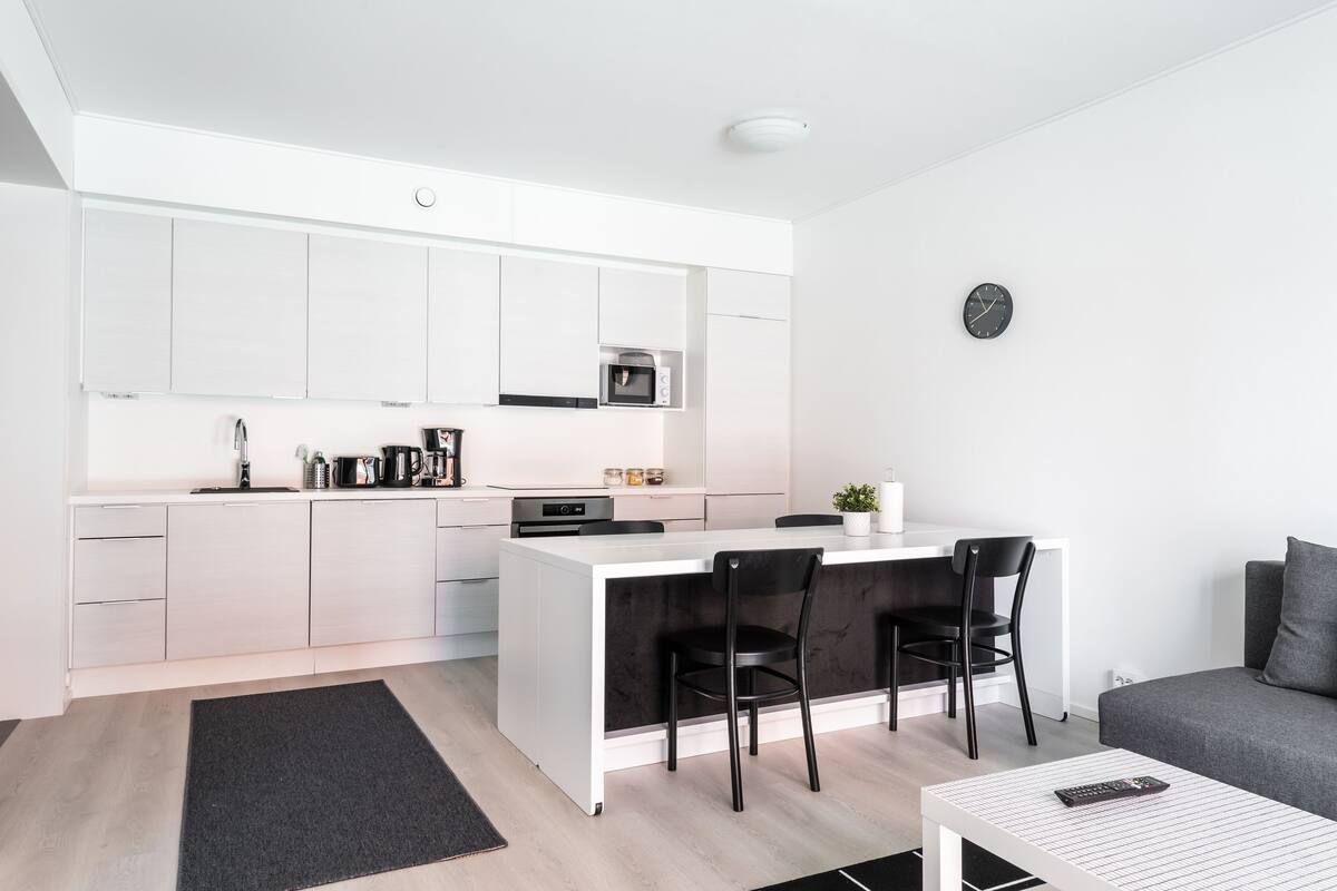 A modern kitchen with white cabinets, a central island with chairs, a microwave, and a coffee maker.