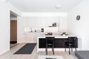 Una cocina moderna con armarios blancos, encimera negra y microondas integrado. Hay dos sillas negras y una pequeña planta en maceta sobre la encimera.