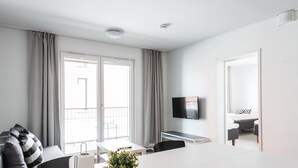 A modern hotel room with a large window, a flat-screen TV, a dining area, and a balcony. - Hiisi Homes Turku Fleminginkatu (Turku)