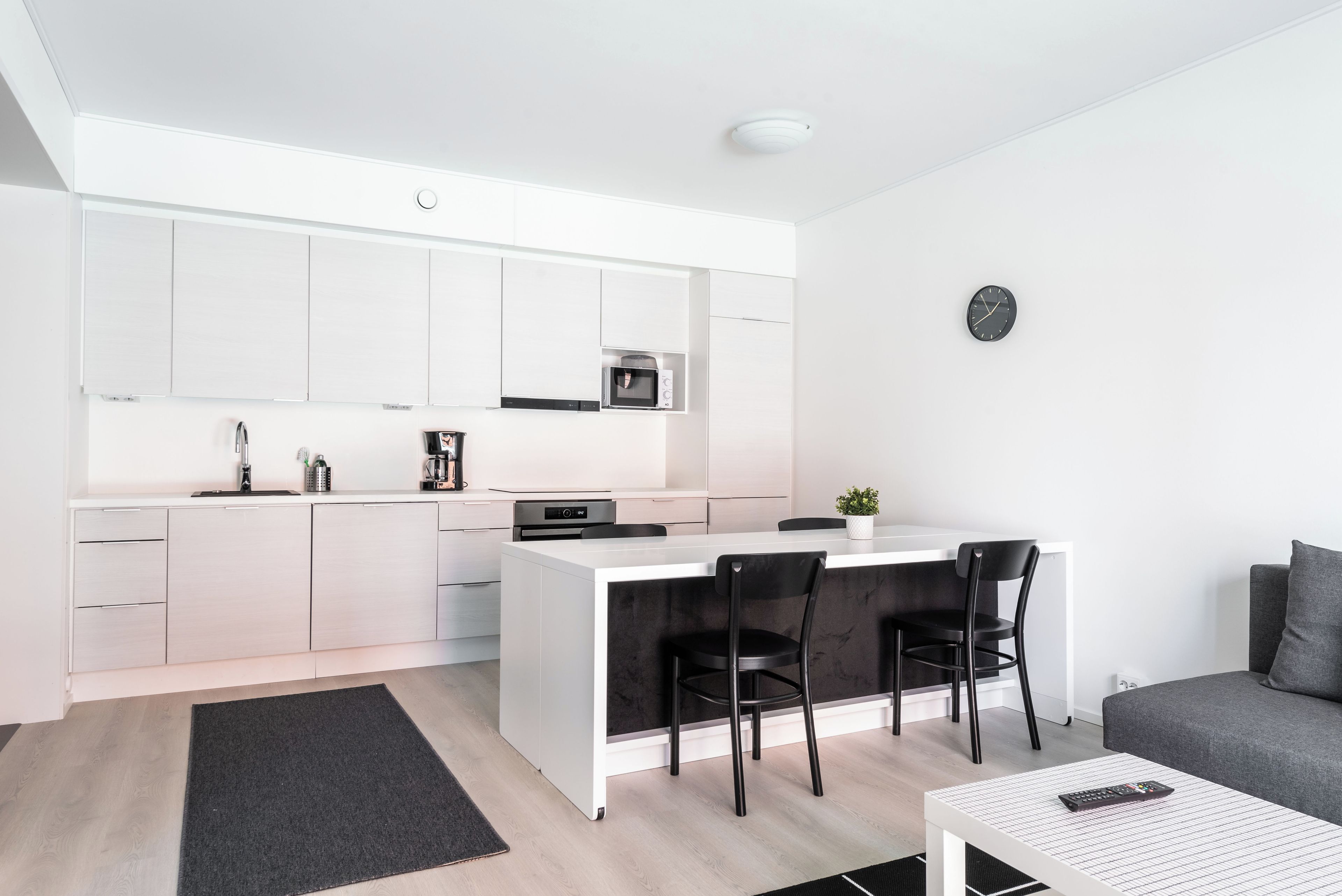 Una cocina moderna con armarios blancos, una isla central y una zona de comedor con sillas negras.