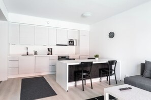 A modern kitchen with white cabinetry, a central island, and a dining area with black chairs. - Hiisi Homes Turku Fleminginkatu (Turku)