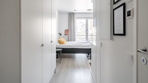 A modern hotel room with a bed, a desk, and a view of the city through large windows. - Hiisi Homes Turku Fleminginkatu (Turku)