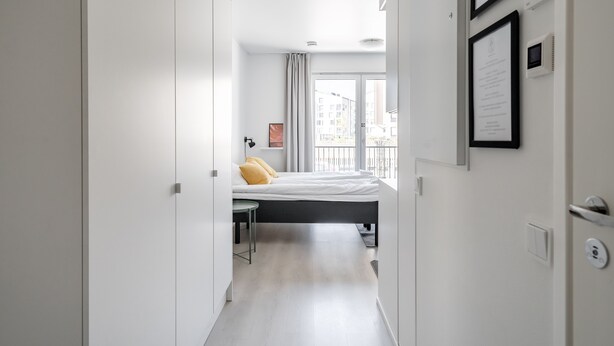 A modern hotel room with a bed, a desk, and a view of the city through large windows. - Hiisi Homes Turku Fleminginkatu (Turku)