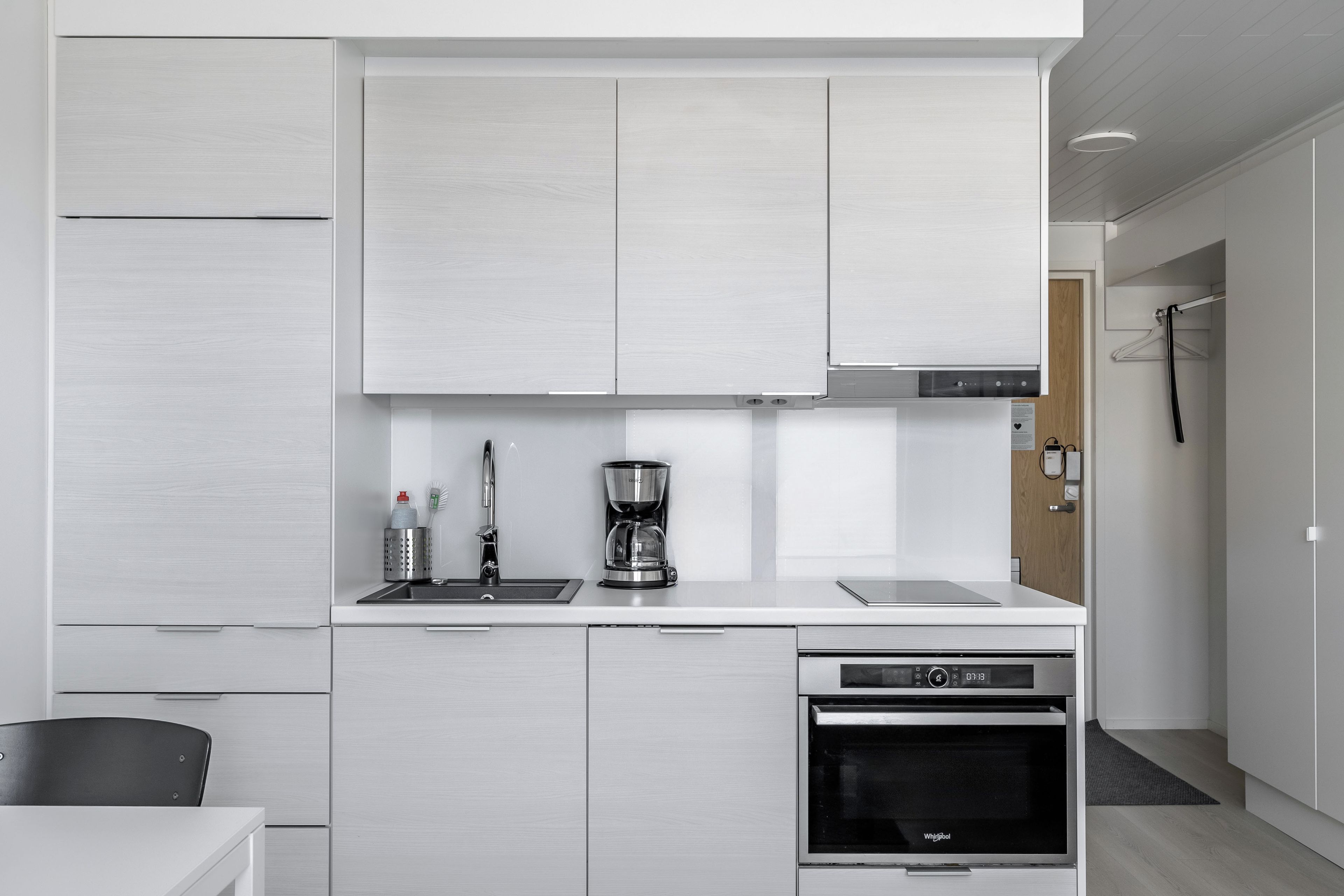 Cozinha moderna com armários brancos, máquina de café e forno embutido.