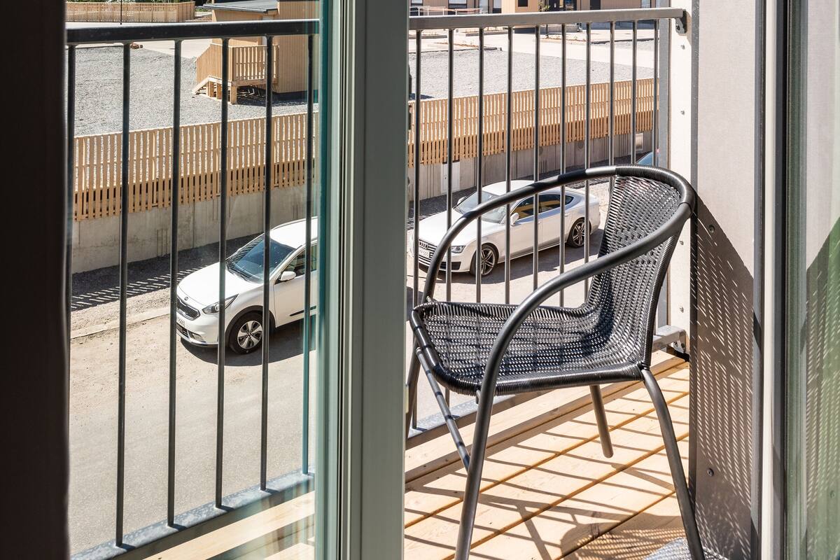 A balcony with a metal chair, a view of a parking lot, and a building in the background.