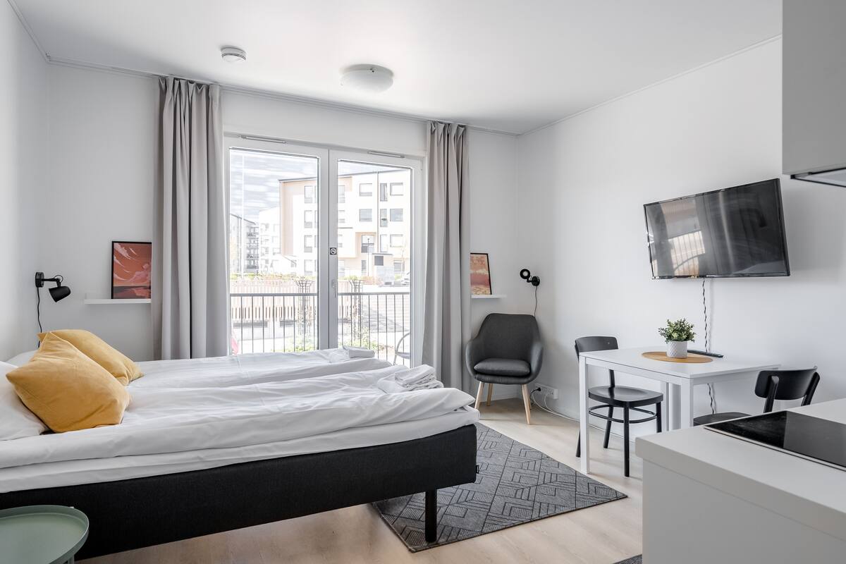 A modern hotel room with a bed, a desk, a chair, a TV, and a view of the outside.
