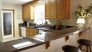 A kitchen with wooden cabinets, a granite countertop, a sink, and a coffee maker. There are three stools and a vase with flowers on the countertop. - Two Master Family Home / Easy to Access Year-Round / Nearby Trails (South Lake Tahoe)