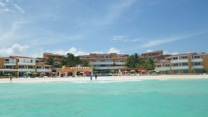 A beachfront hotel with multiple balconies, beach umbrellas, and palm trees. - Beach Resort, Playa Del Carmen, Mexico, Spectacular View! 333S (Playa del Carmen, QRO)