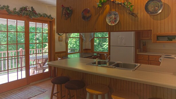 Een keuken met houten lambrisering, een groot eiland met krukken, een koelkast en uitzicht door de ramen.