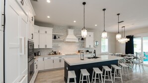A modern kitchen with white cabinets, a large island with bar stools, and pendant lighting.